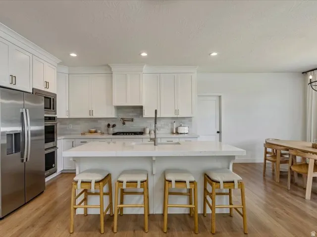Kitchen featuring white cabinetry, stainless steel appliances, a center island with countertop seating, wood-finish flooring, and recessed lighting