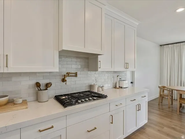 White shaker cabinetry with brass hardware, light-toned countertops, subway tile backsplash, and wood-finish flooring