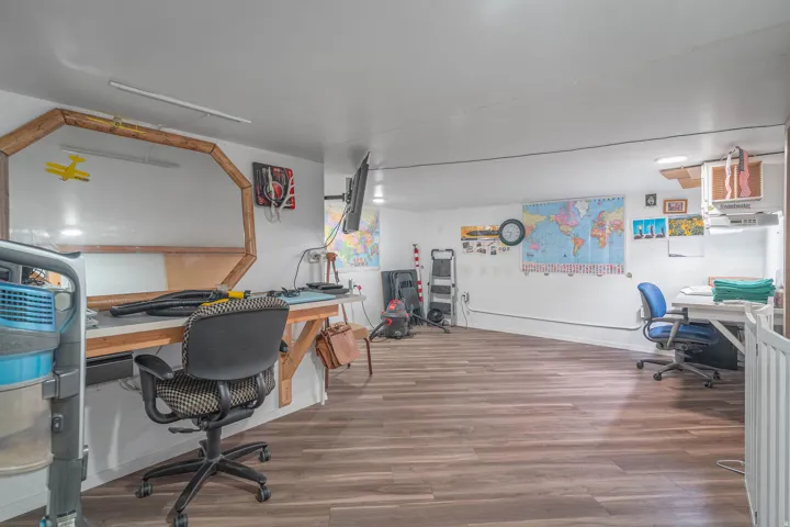 Spacious room featuring wood-finish flooring, white walls, and multiple built-in workstations