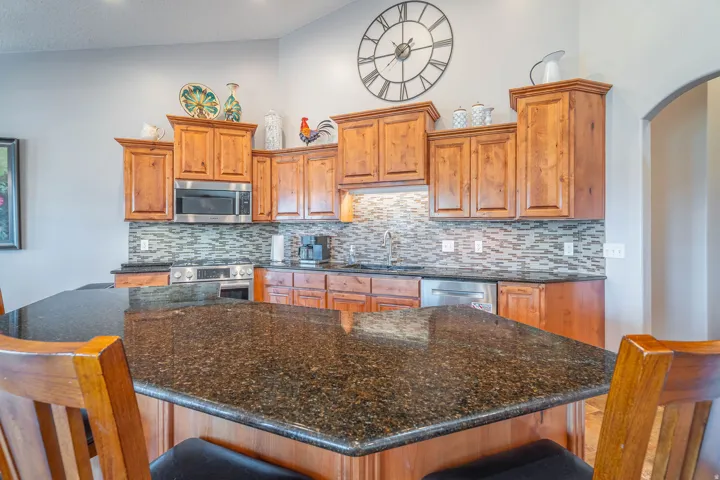 Kitchen featuring a dark granite island, wood-finish cabinetry, stainless steel appliances, a mosaic tile backsplash, and an arched entryway