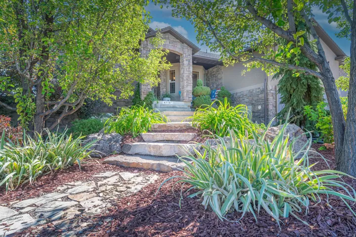 Stone facade residence with a covered entry, natural stone steps, mature trees, and landscaped garden beds