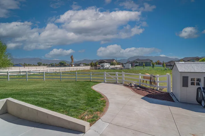 Expansive green lawn with a white fence, curved concrete pathway, and a white storage shed