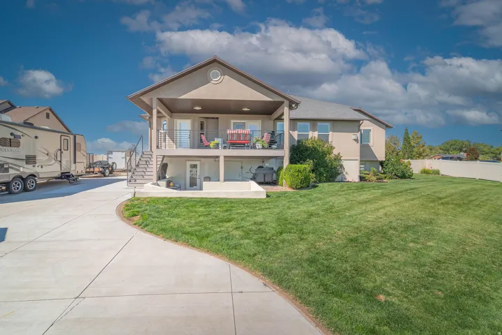 Stucco exterior with a covered upper balcony, lower patio, and a spacious lawn area