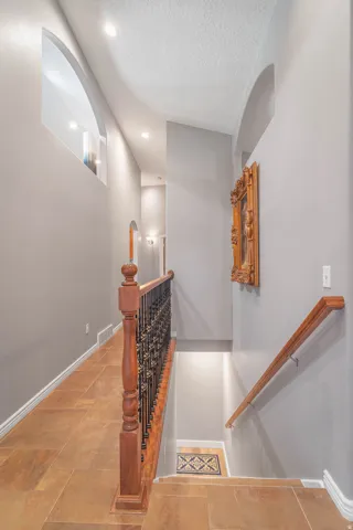 Tiled flooring leading to a staircase with wood railing and wrought iron balusters