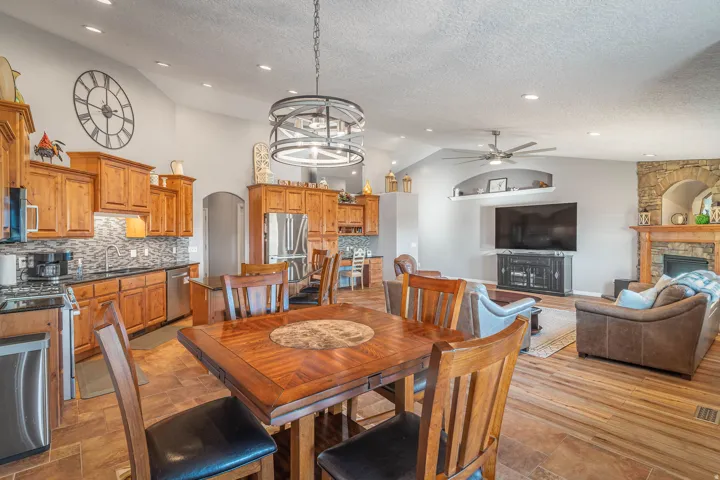 Vaulted ceilings with recessed lighting, stone-clad fireplace, wood-finish flooring, and a kitchen featuring wood cabinetry and stainless steel appliances