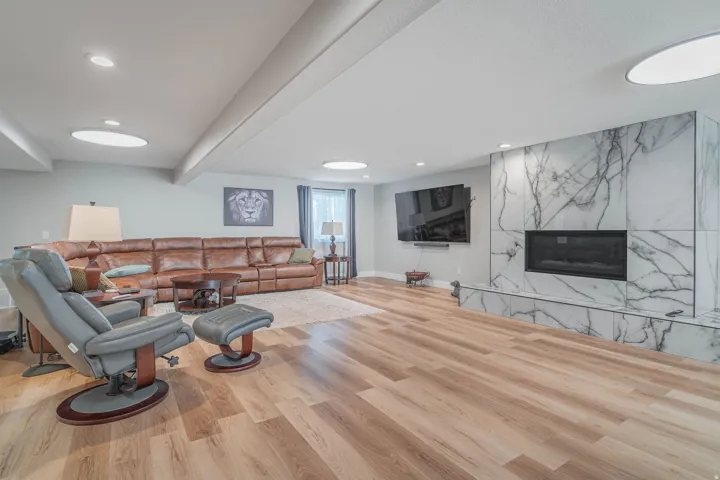 Spacious room featuring wood-finish flooring, recessed lighting, and a fireplace with a stone surround