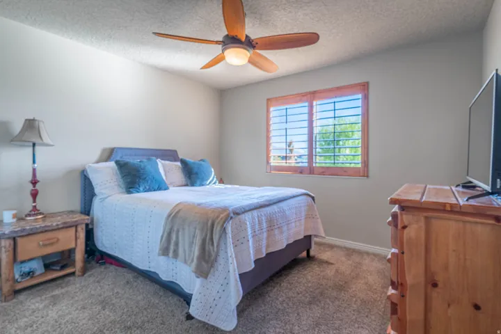 Carpeted flooring, a ceiling fan with integrated lighting, and a window with wood-frame shutters