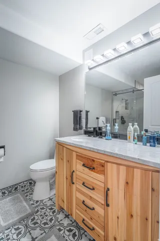 Light wood-finish vanity with a stone countertop, under-mount sink, and a large wall-mounted mirror