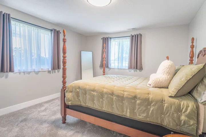 Neutral wall paint, ceiling-mounted light fixture, two windows with curtain rods, and carpeted flooring
