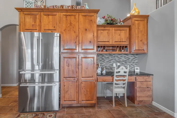 Built-in desk with dark countertop, wood-finish cabinetry, and mosaic tile backsplash