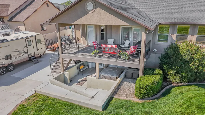 Multi-level outdoor living space featuring a covered upper deck, a lower concrete patio with built-in hot tub, and a concrete driveway