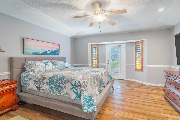 Tray ceiling with a ceiling fan, wood-finish flooring, and a glass-paneled exterior door flanked by two windows with louvered shutters