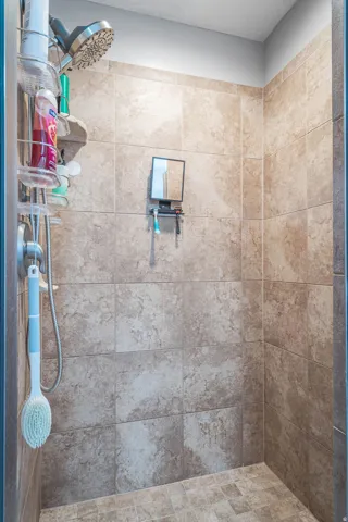 Tile shower with a handheld shower fixture and a built-in corner shelf