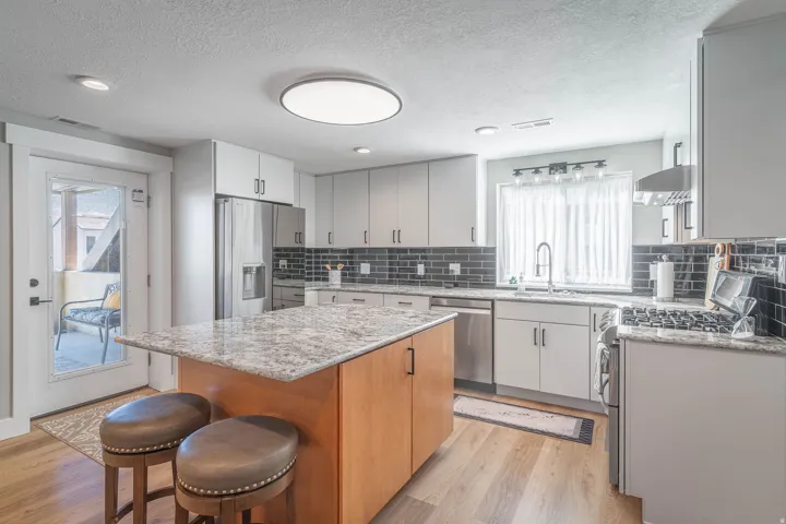 Gourmet kitchen featuring a central island with a stone countertop, light wood-finish flooring, stainless steel appliances, and sleek gray cabinetry