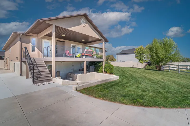 Two-story stucco exterior with covered upper deck, lower patio area, concrete driveway, and expansive lawn