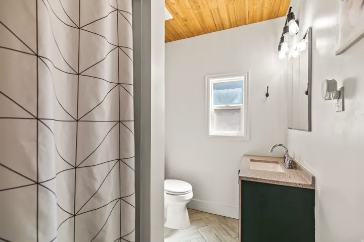 Wood-finish plank flooring, wood-paneled vaulted ceiling, corner vanity with undermount sink, and wall-mounted vanity lighting