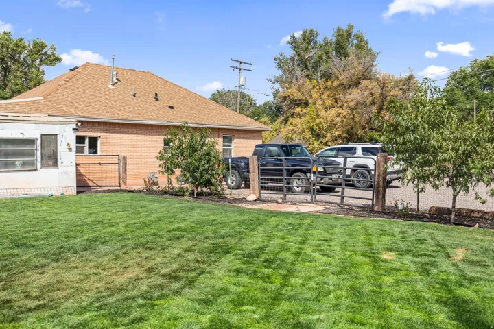 Expansive green lawn with a brown shingled roof, brick exterior, and a metal fence