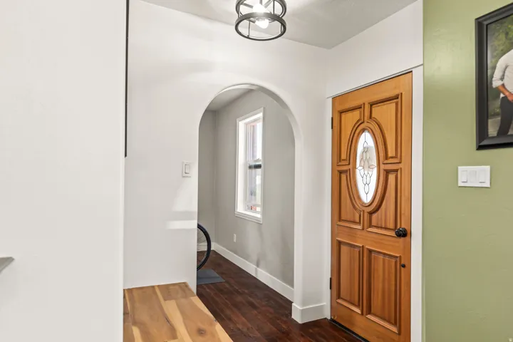 Solid wood entry door with oval leaded glass insert, arched hallway opening, and dark wood-finish flooring