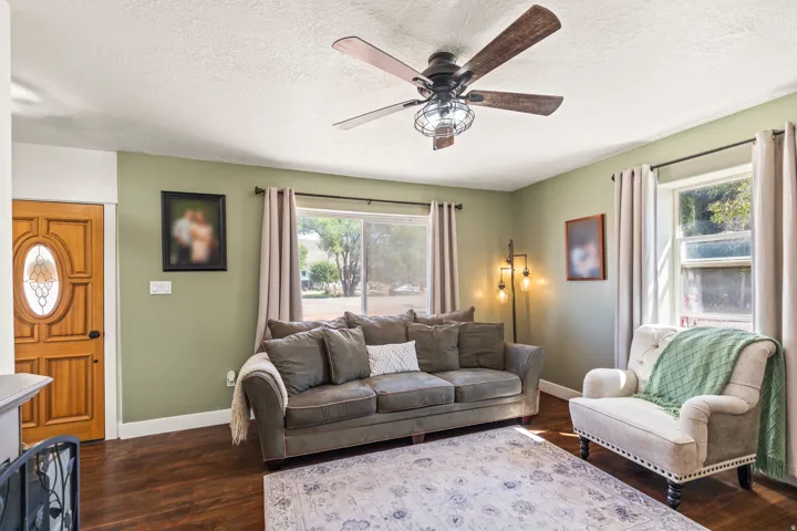 Wood-finish flooring throughout, ceiling fan with integrated lighting, recessed windows with curtain rods, and a paneled wooden door with an oval stained-glass insert