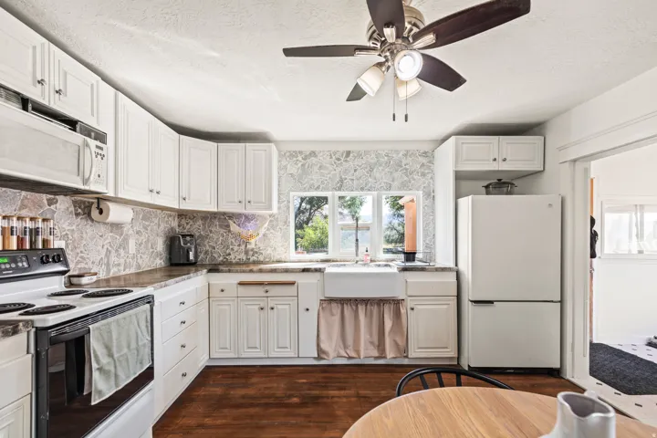Kitchen featuring white cabinetry, stone-finish backsplash, wood-finish flooring, a farmhouse sink, and a ceiling fan with integrated lighting