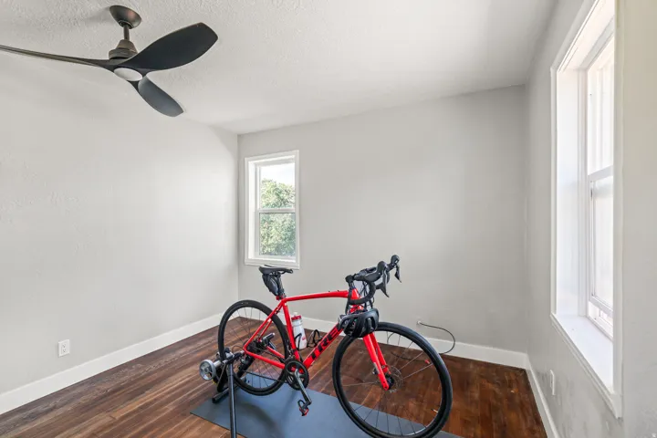 Room featuring wood-finish flooring, white walls, two window openings, and a ceiling fan