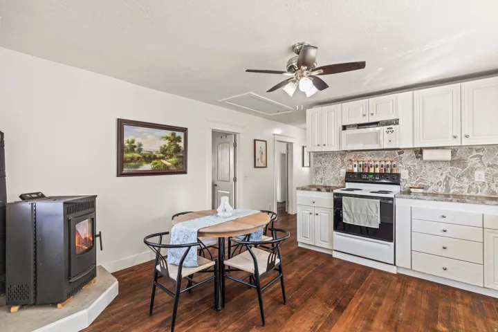 Wood-finish flooring, white cabinetry, integrated microwave, range oven, and a ceiling fan with integrated lighting