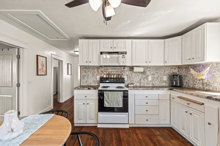 White cabinetry, wood-finish flooring, stone-look countertops, and a stone-look backsplash