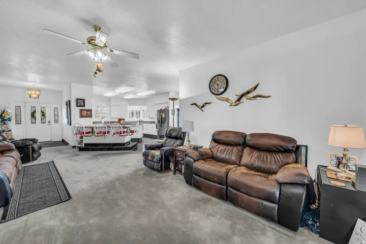 Spacious interior with neutral carpeting, a brass-tone ceiling fan with integrated lighting, and white walls