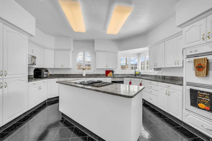 Expansive kitchen featuring white cabinetry, dark stone countertops, a central island with cooktop, and integrated double wall ovens