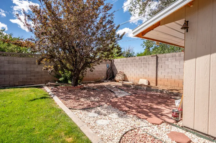 Backyard featuring a mature tree, paver and gravel hardscaping, a concrete block privacy wall, and a grass lawn