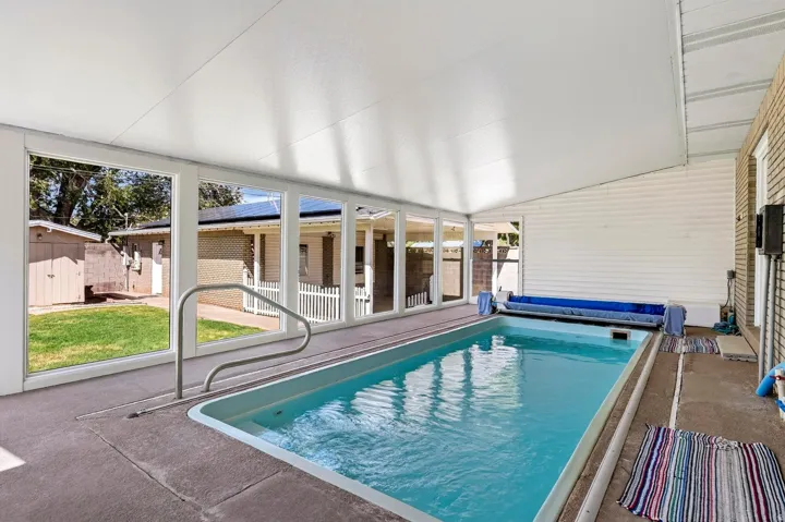 Enclosed swimming pool with a concrete surround and integrated handrails, featuring full-height windows and a covered ceiling
