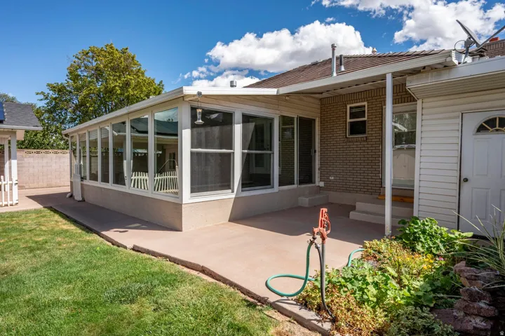 Expansive concrete patio with a sunroom addition, brick exterior accents, and a manicured lawn