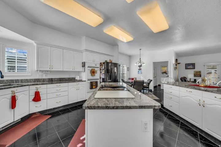 Extensive white cabinetry, dark stone countertops, black tile flooring, integrated double oven, and recessed lighting