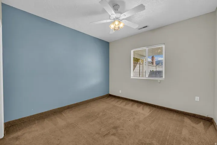 Carpeted room featuring a ceiling fan with integrated lighting, a sliding window, and two-tone wall paint