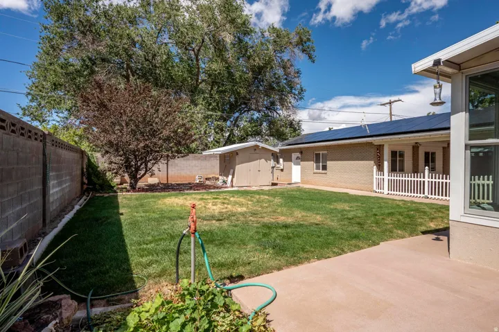 Expansive backyard featuring a manicured lawn, established trees, concrete patio, and privacy wall