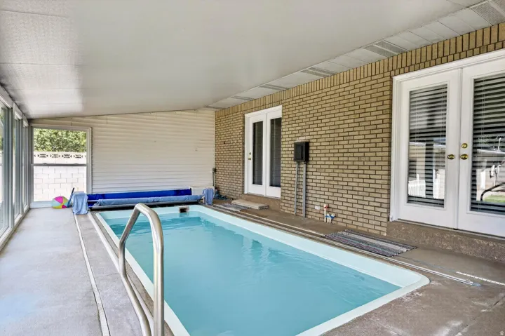 Indoor swimming pool with concrete decking, brick wall, and multiple white-framed double doors