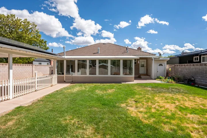 Expansive grassy yard area with a paved walkway, covered carport structure, and a white picket fence