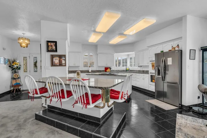 Kitchen featuring white cabinetry, dark tile flooring, stainless steel refrigerator, recessed lighting, and a multi-level breakfast bar with integrated seating