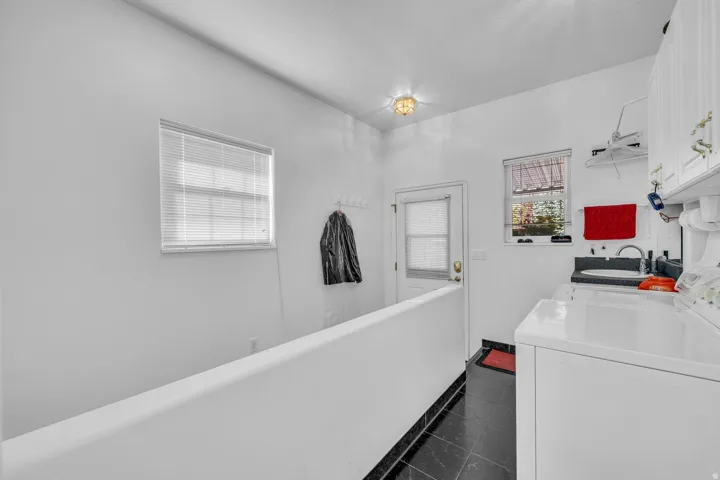 Tile flooring with a half-wall partition, white cabinetry, and a utility sink