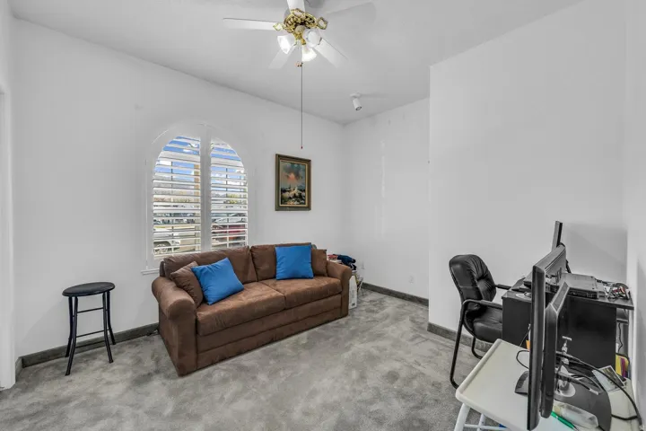 Arched window with plantation shutters, ceiling fan with integrated lighting, and gray carpeting