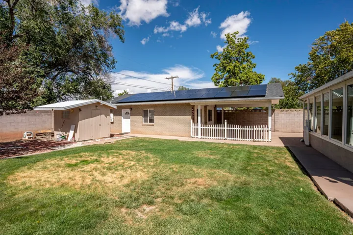 Brick exterior with solar panels, covered patio with white picket railing, detached shed, and an adjacent enclosed sunroom