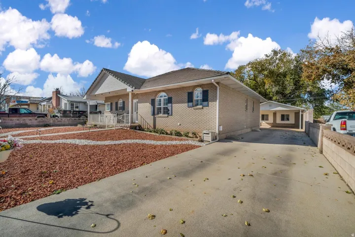 Brick exterior with white siding accents and dark shutters, front porch with white railings, concrete driveway, decorative rock landscaping, and a detached carport