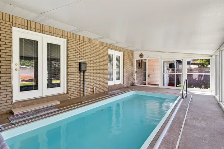 Indoor swimming pool with concrete decking, surrounded by brick walls and multiple sets of glass-paneled double doors