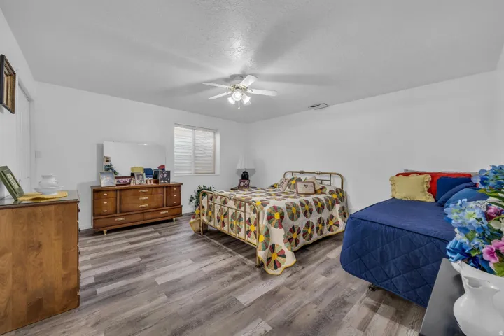 Spacious room featuring wood-finish flooring, white walls, a ceiling fan, and a window with horizontal blinds
