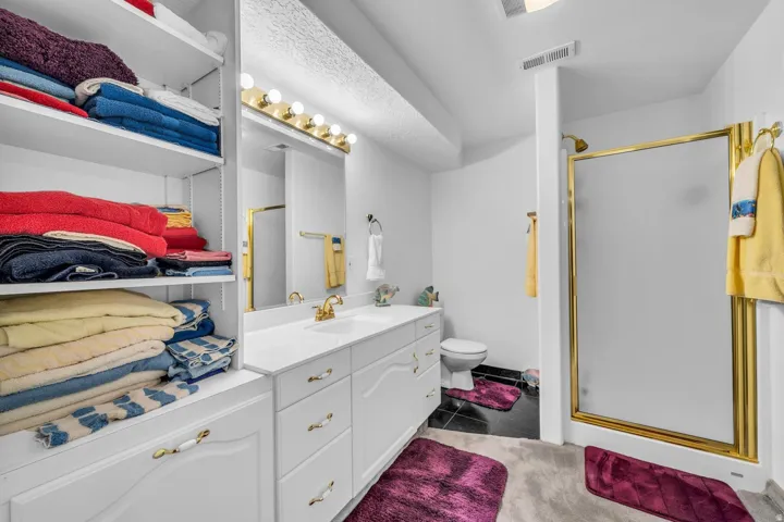 Double vanity with white cabinetry, ample storage shelving, and a glass-enclosed shower