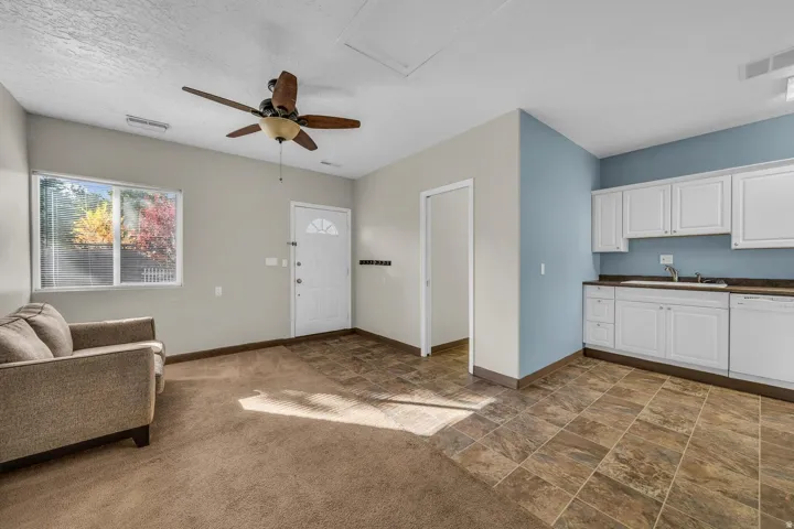 Open-concept area featuring light-toned walls, a ceiling fan, and a mixed flooring of carpet and tile
