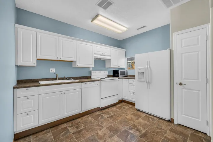 White cabinetry, dark countertops, a white built-in dishwasher, and an electric range