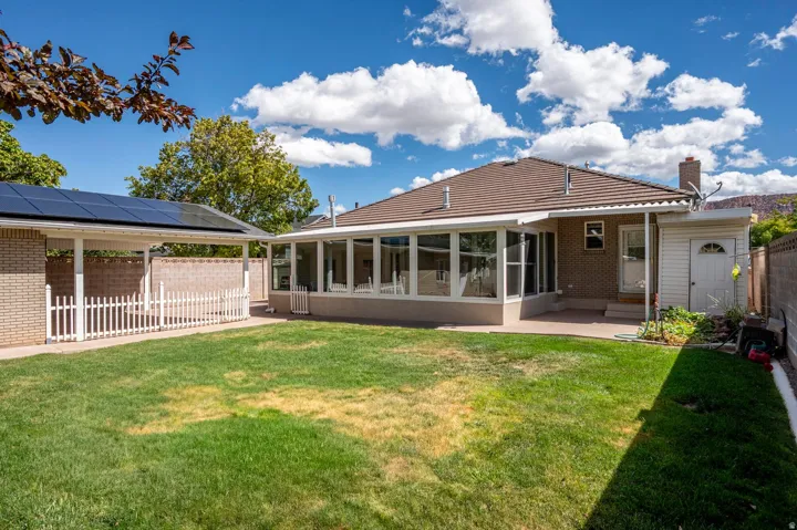 Expansive backyard featuring a sunroom, covered patio, and a separate structure with solar panels