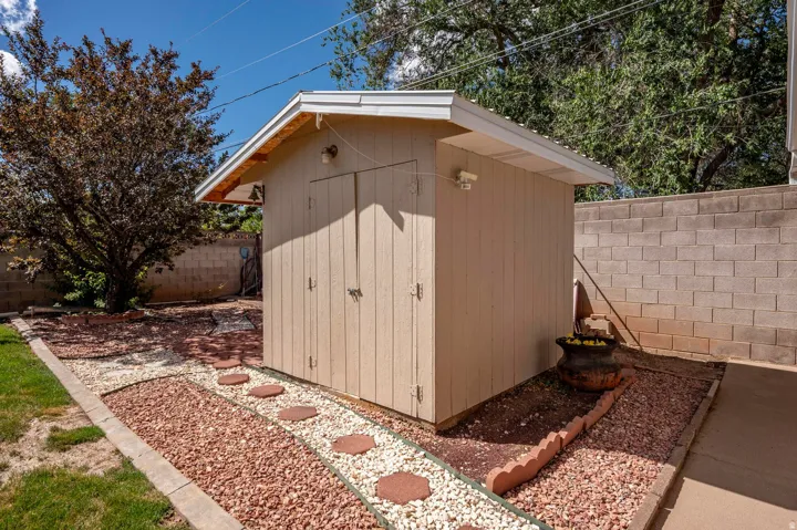 Detached storage shed with a gable roof, concrete block perimeter wall, a decorative rock pathway, and mature landscaping
