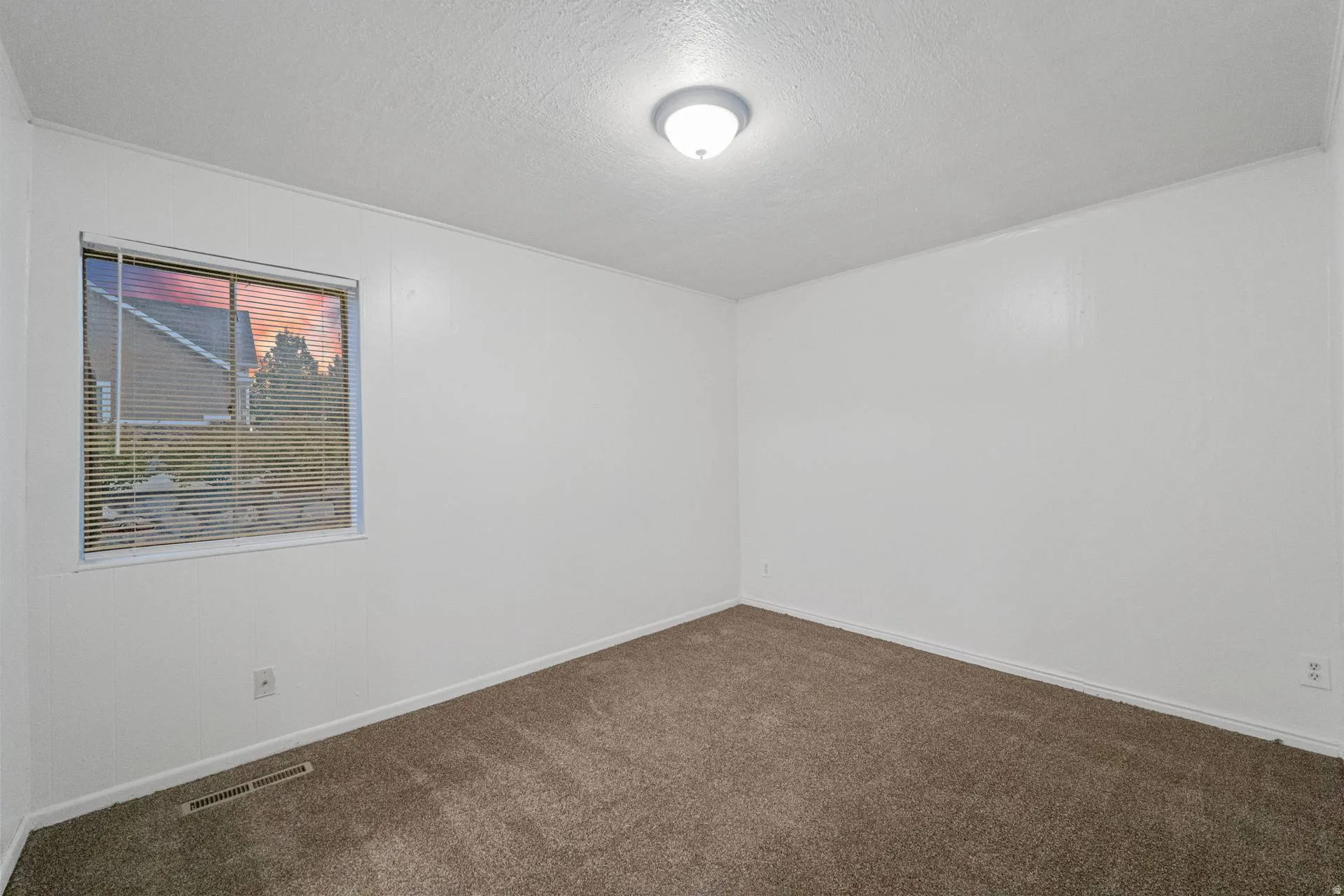 Crisp white walls, neutral carpet, flush-mount ceiling light fixture, and window with blinds